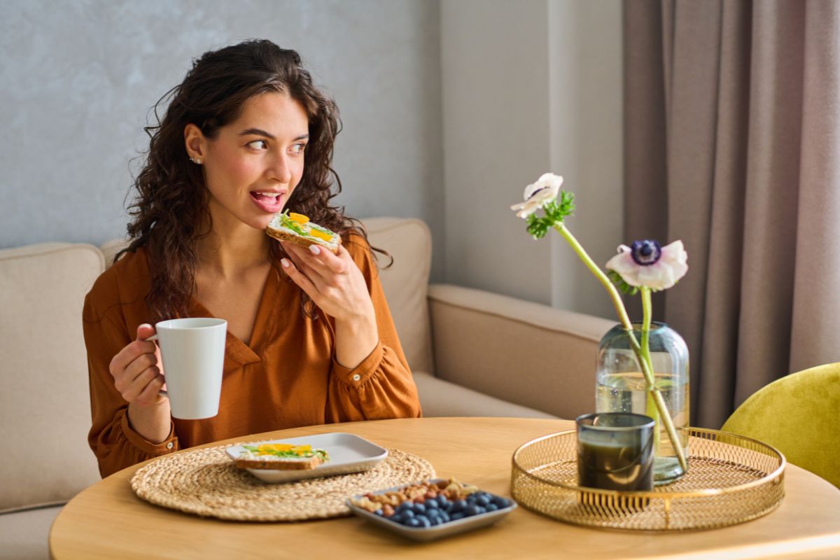 5 Fresh Snack Ideas Woman eating healthy food at dining table with flowers and water glass indoors.
