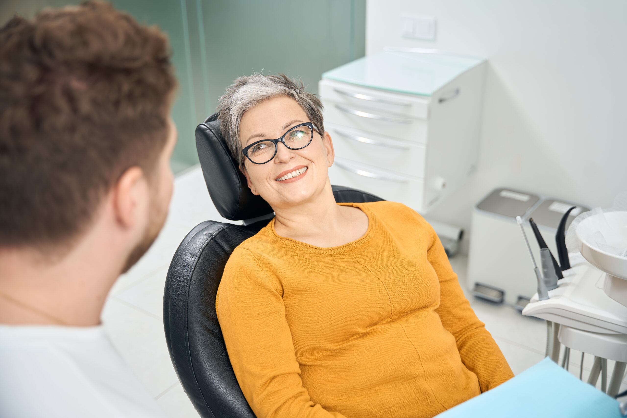 Adult woman showing her toothy smile to qualified dentist doctor Adult patient smiling comfortably while speaking with a dentist during a routine dental visit