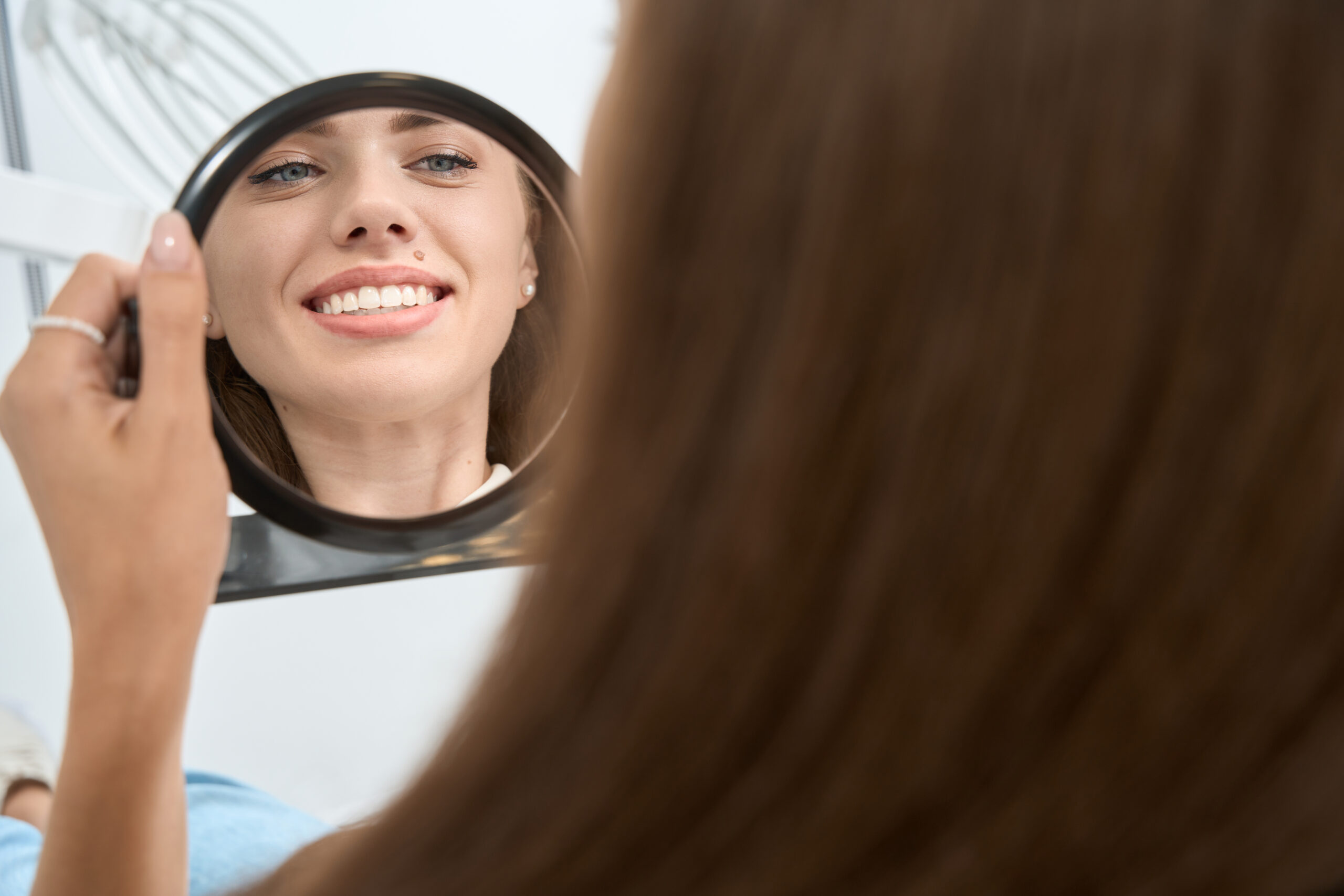 Dental clinic client admiring her clean white teeth Patient smiling while looking at her teeth in a mirror after cosmetic dental treatment