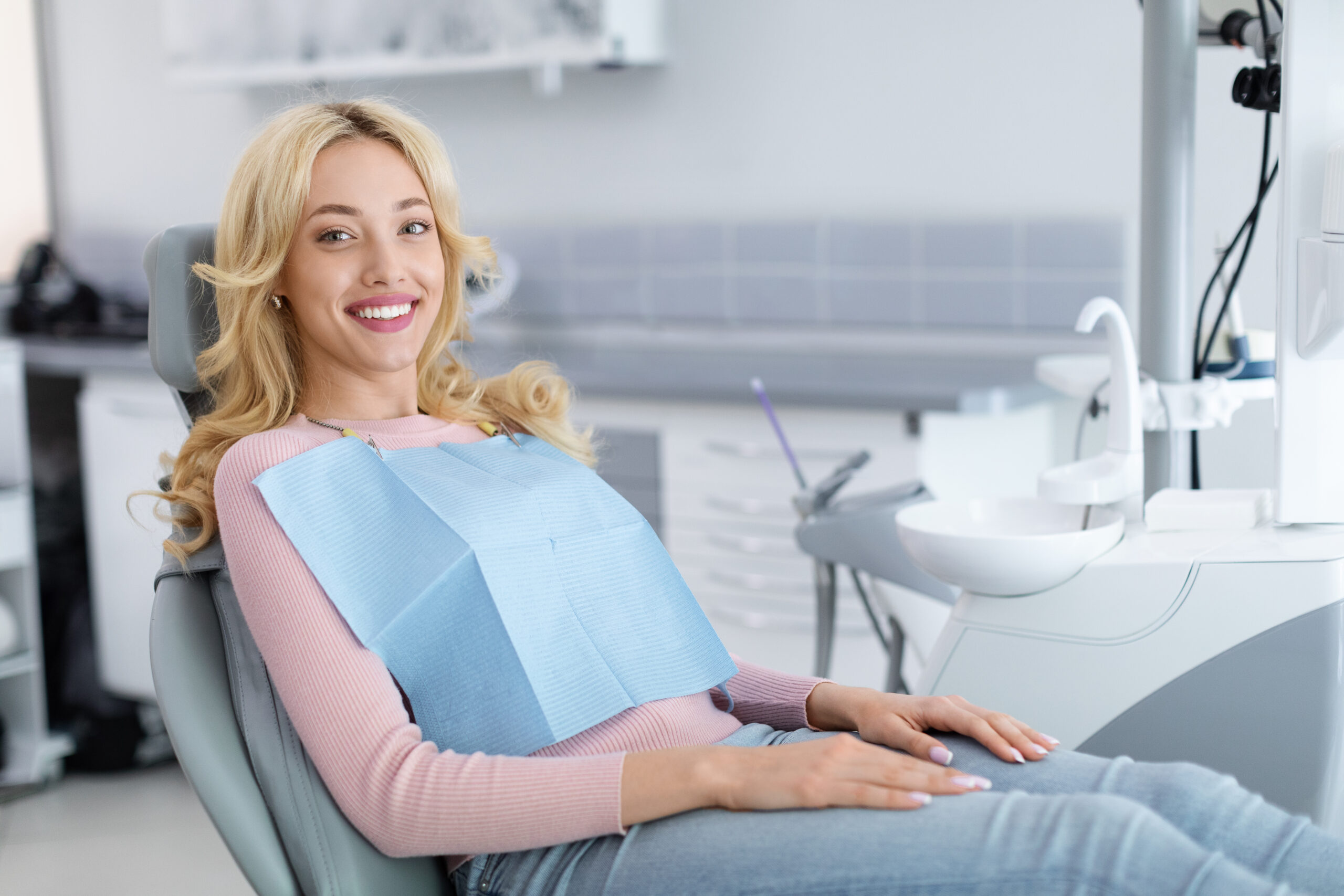 Blonde young woman patient smiling in dentistry, copy space Older adult patient smiling comfortably during a routine dental visit in a modern dental office