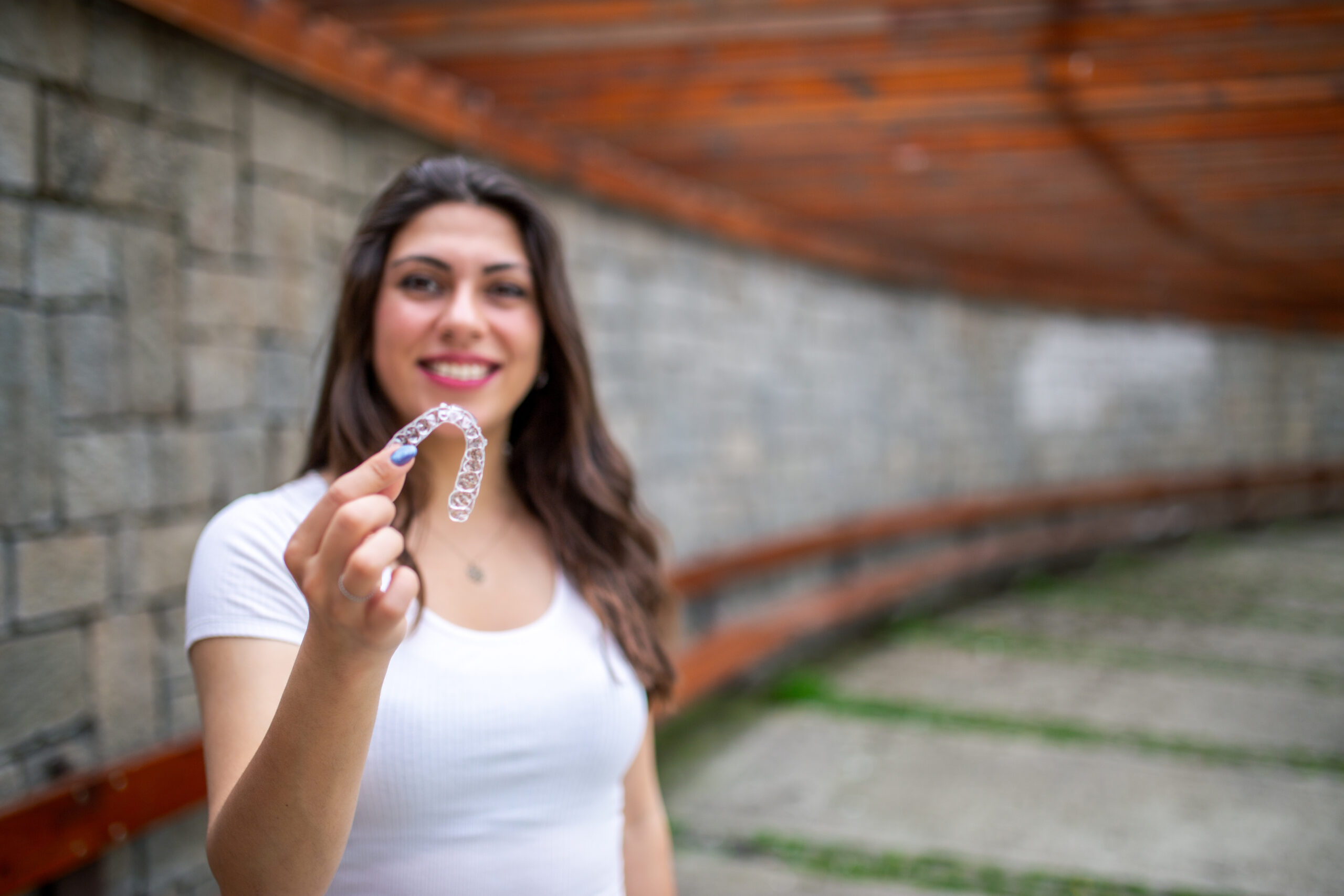 Woman holding a clear aligner tray and smiling, representing Invisalign treatment for discreet teeth straightening