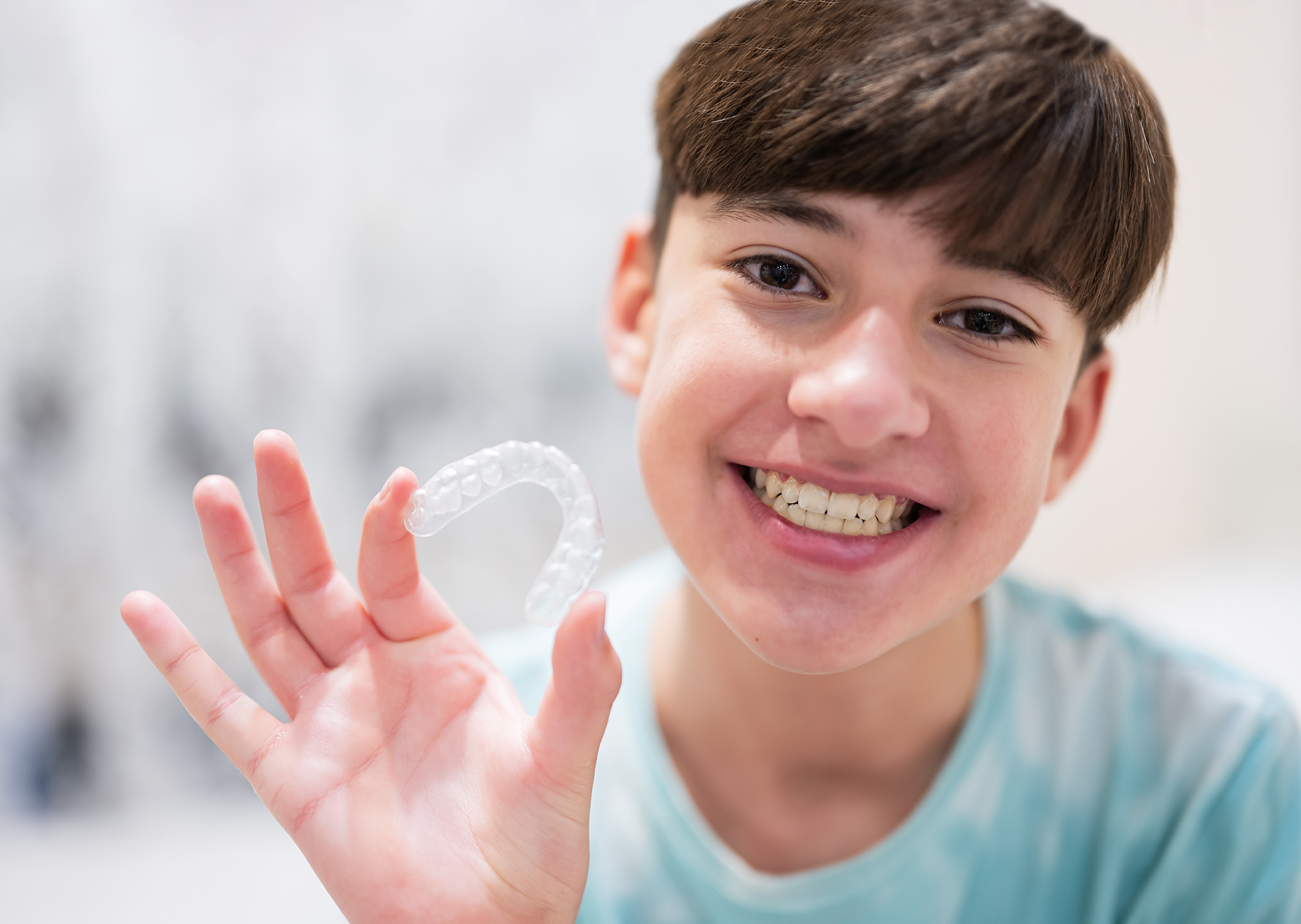 Teenager boy wear simulator orthodontic silicone invisible level Teen smiling while holding a clear aligner tray for Invisalign treatment