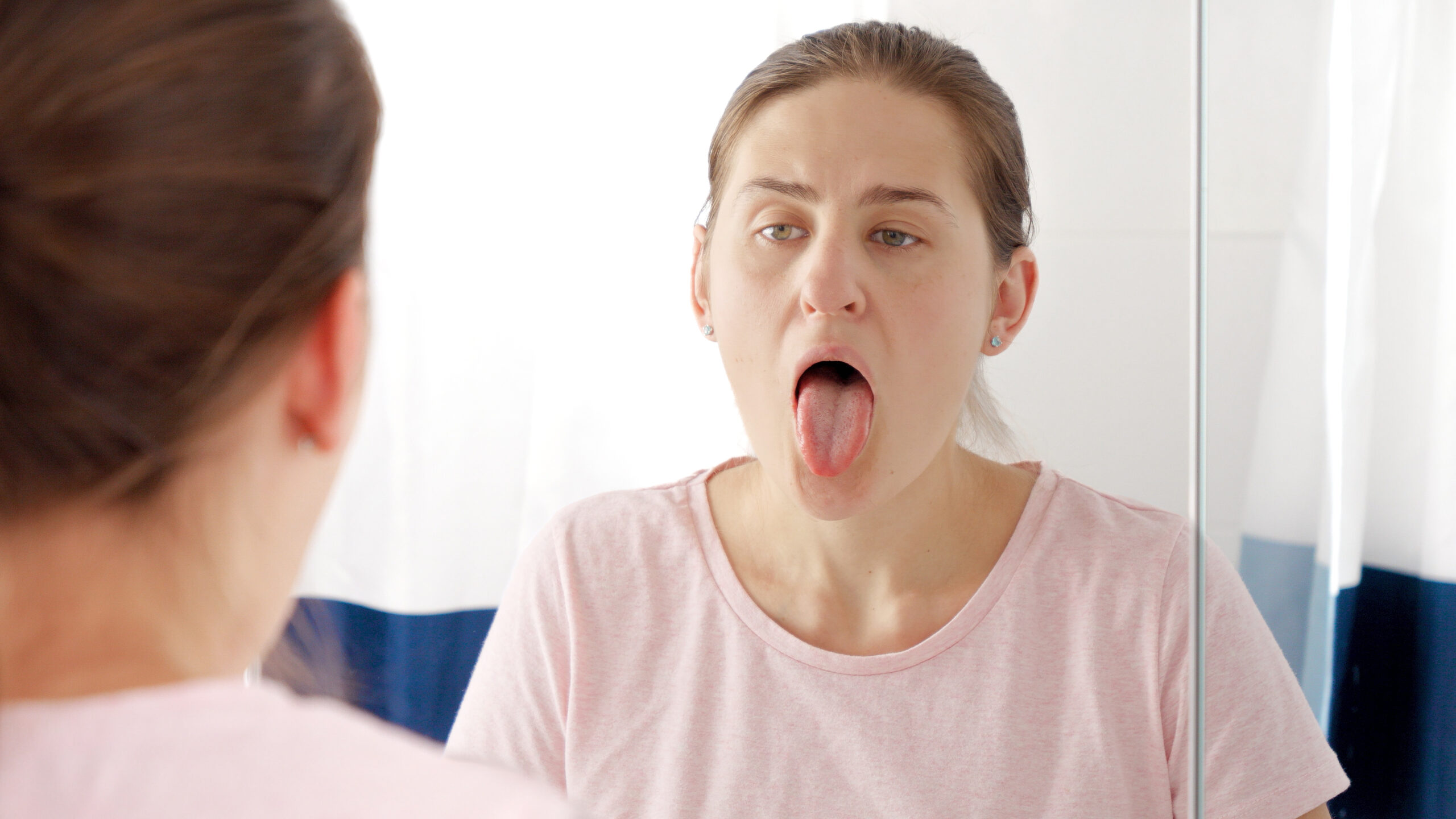 Woman checking her tongue in the mirror for signs of oral health changes